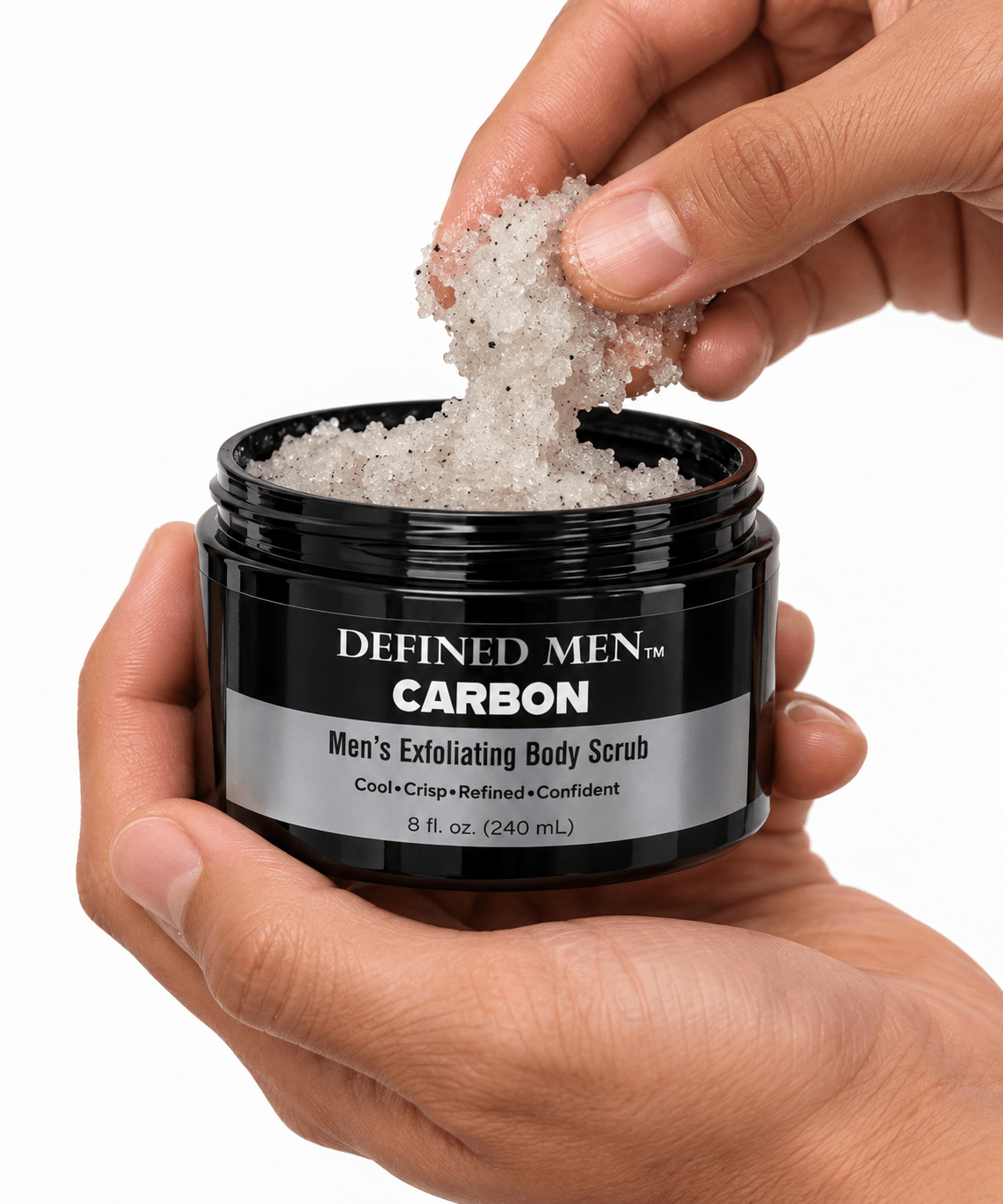 A hand scooping Omnia Bene Defined Men Carbon exfoliating body scrub from its black jar.