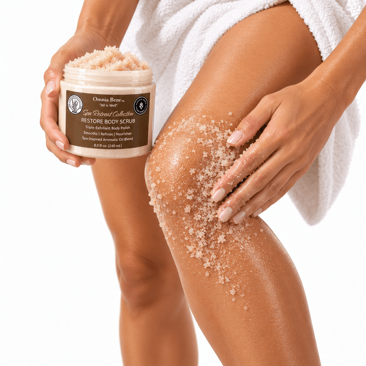 Omnia Bene RESTORE Body Scrub massaged over a knee and leg, with the jar held alongside.