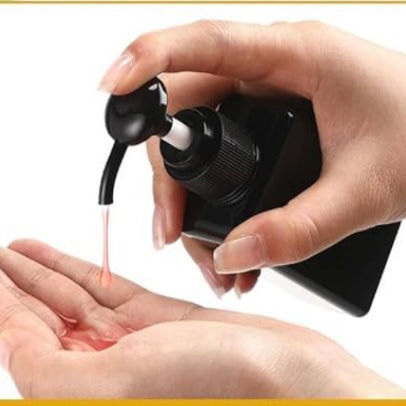 Hand using a black pump bottle to dispense  lotion onto another hand against a white background