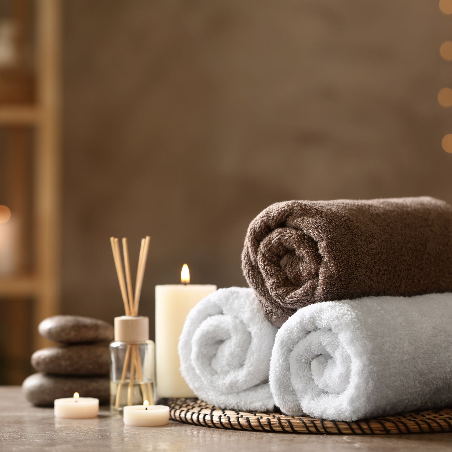 Spa scene with  stack of towels with candles and diffuser on a wooden surface