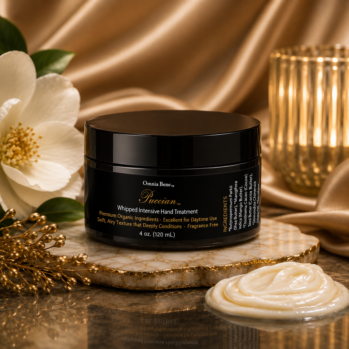 A black jar of Omnia Bene Whipped Intensive Hand Treatment sits on a marble slab with a swirl of cream product in front, styled with a white flower, gold leaf, and draped gold silk fabric in the background. Dry, rough, skin support. Daytime hand cream. Whipped, airy, Shea, Mango and Cocoa Butter plus Botanical Oils included in Whipped Intensive Hand Treatment. Fragrance Free. Organic Ingredients.