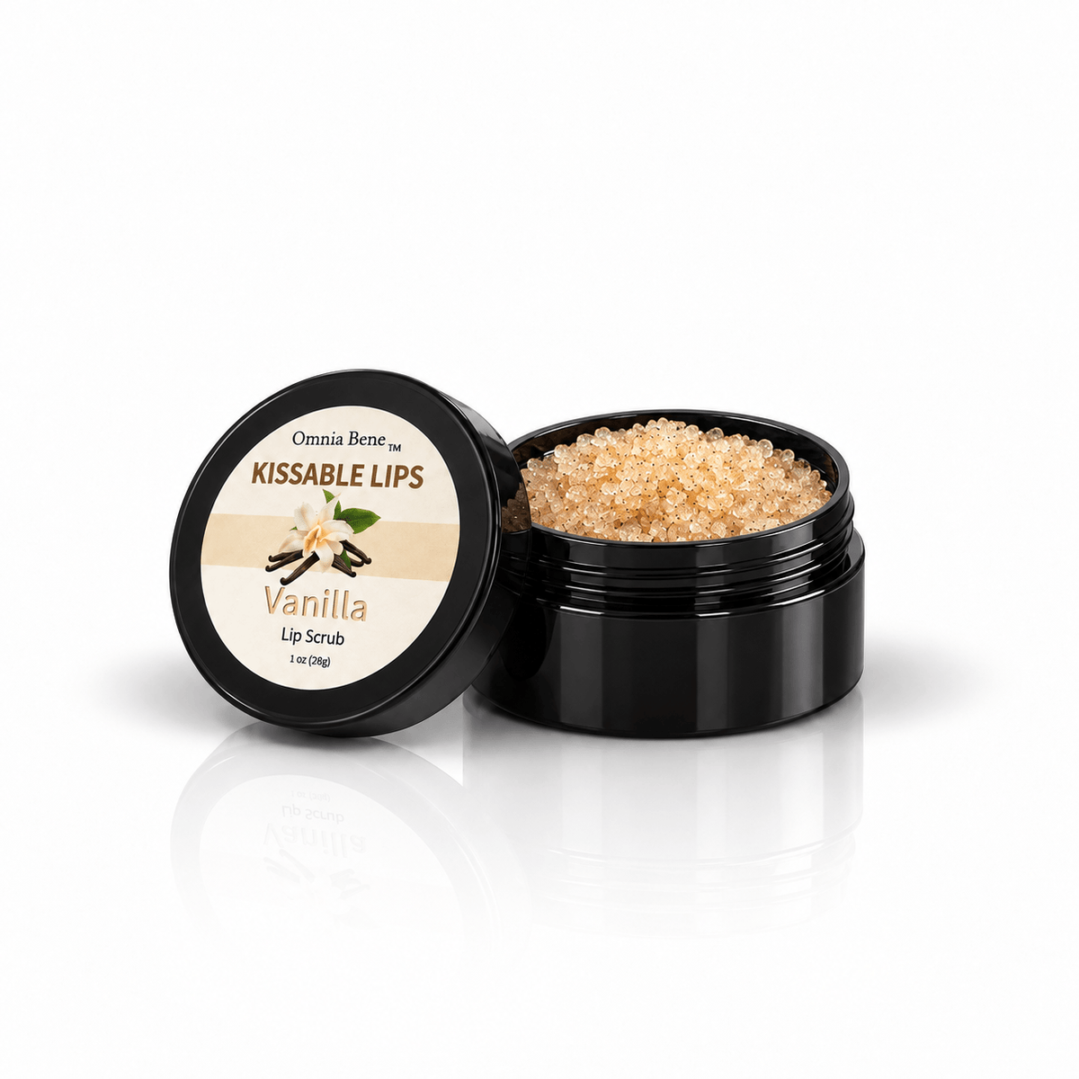 Omnia Bene Kissable Lips Vanilla Lip Scrub, a 1 oz black jar opened to show the sugar granules inside. A 1 oz black jar of sugar lip exfoliant that smells like vanilla birthday cake. Gentle enough for everyday use - it smooths rough, dry, flaking lips in seconds. Follow with an Omnia Bene lip balm to seal the softness in.