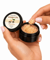 A fingertip lifting sugar scrub from an open jar of Omnia Bene Kissable Lips Vanilla Lip Scrub.