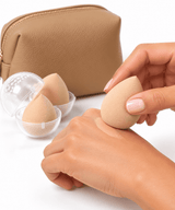 An Omnia Bene makeup sponge blending foundation on the back of a hand, beside clear protective sponge cases.