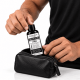 A man placing Omnia Bene Carbon Body Lotion into a black leather toiletry case.