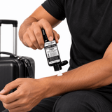 A man holding Omnia Bene Carbon Body Lotion beside a suitcase, packing for travel.