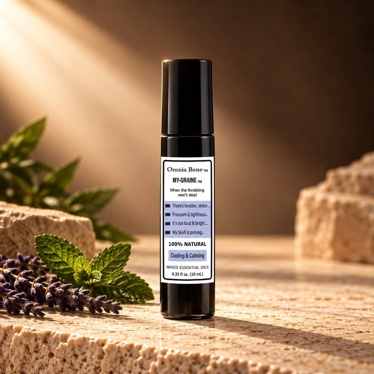 Omnia Bene MY-GRAINE rollerball on sunlit stone beside fresh mint and lavender.