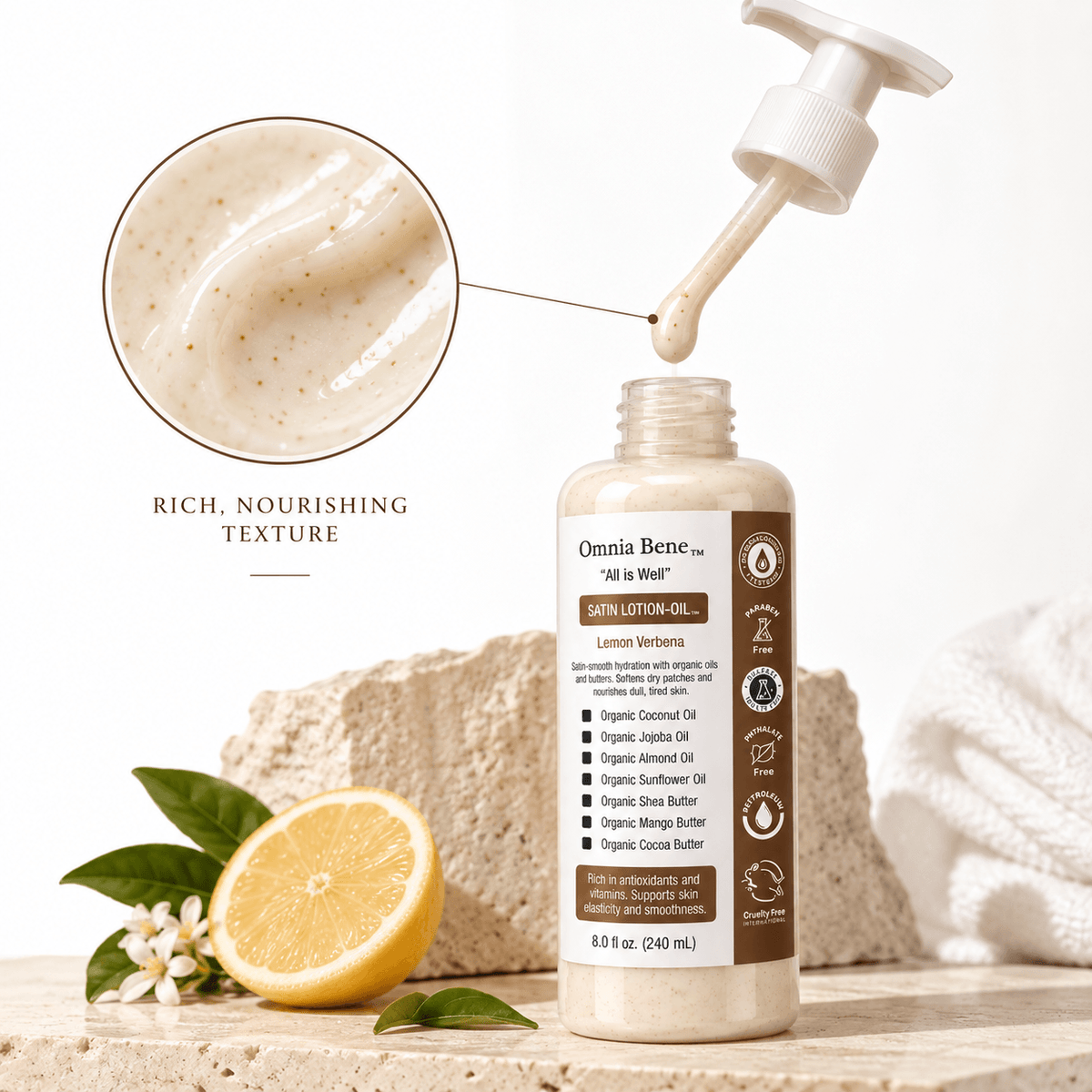 Omnia Bene Satin Lotion-Oil on a stone ledge with fresh lemon and blossom, beside a swatch of its rich texture.