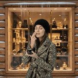 A woman in winter clothing holding a jar of Omnia Bene Puccian Intensive Restorative Hand Treatment outdoors.