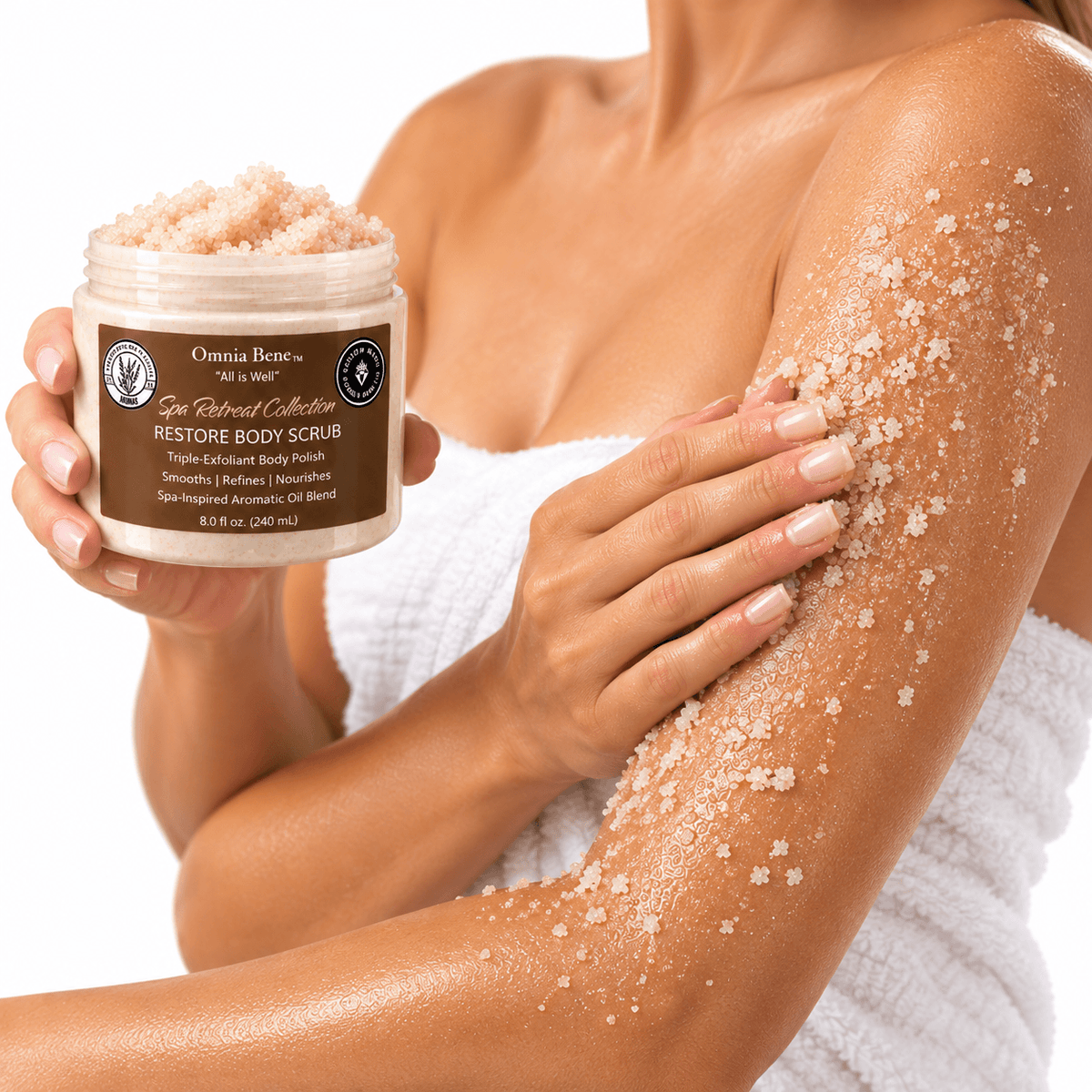 Omnia Bene RESTORE Body Scrub held beside an arm coated in the sugar and salt polish.