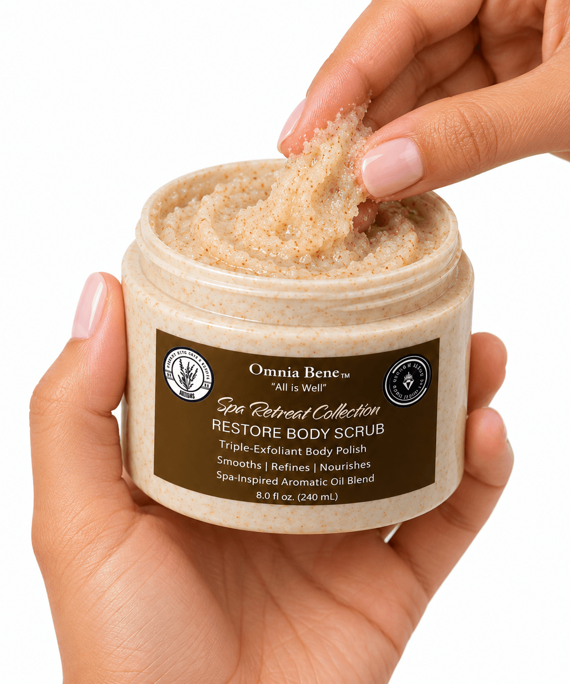A hand scooping Omnia Bene RESTORE Body Scrub from its Spa Retreat Collection jar.