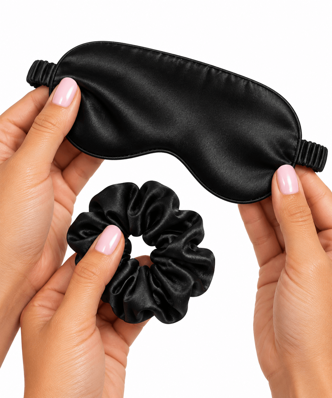 Hands holding an Omnia Bene black satin eye mask and matching satin scrunchie hair tie.