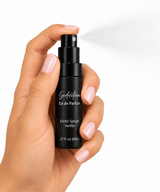 A hand spraying Omnia Bene Seduction exotic spiced vanilla eau de parfum from its 8 mL travel bottle.